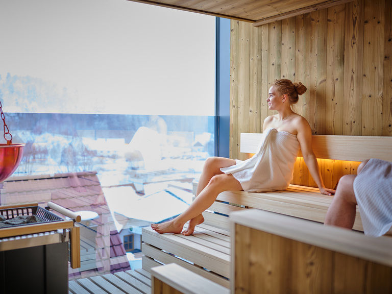 Eine Frau blickt aus dem großen Fenster der Sauna.