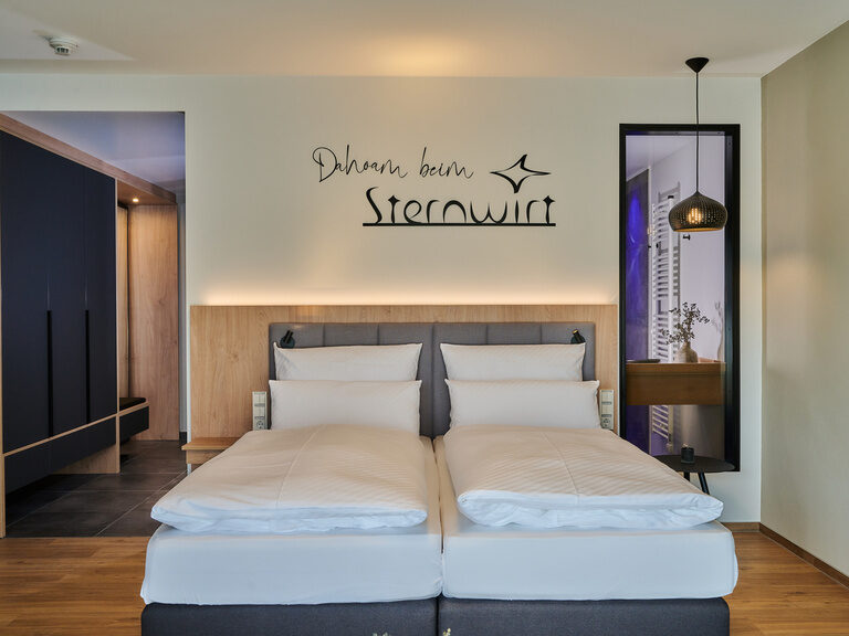 Zwei gemütliche Betten im einladenden Hotelzimmer mit geöffneter Tür.