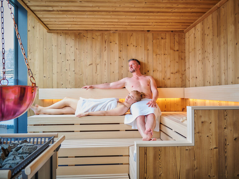 Ein Paar genießt ihren Urlaub in der Sauna mit Ausblick.