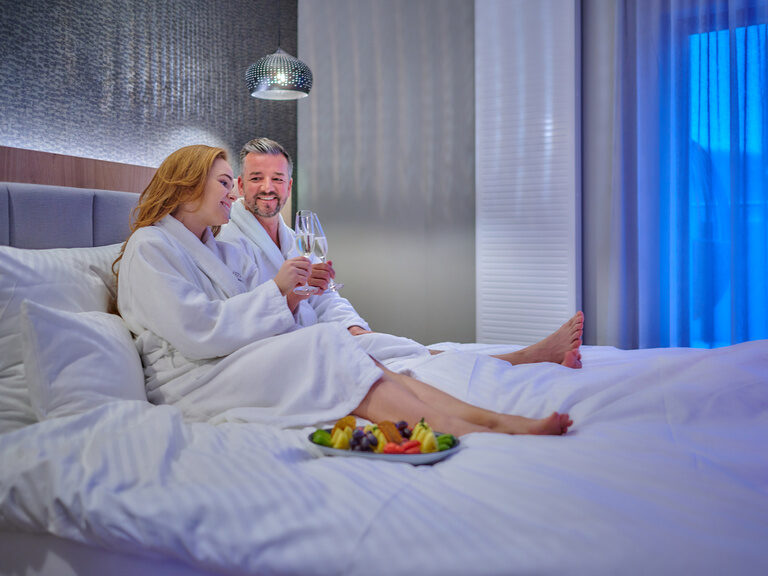 Ein Paar liegt im Bett und stößt mit Sekt an.